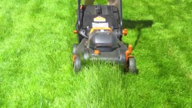 Bir banliyö evinde, yemyeşil çimenler elektrikli çim biçme makinesi kullanılarak titizlikle biçilir, iyi manikürlü ve davetkar bir dış mekan yaratır..