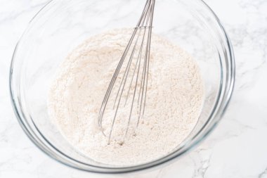 Limonlu haşhaş tohumlu kek pişirmek için bardakta çırpma kabıyla kuru malzemeyi karıştırıyorum..