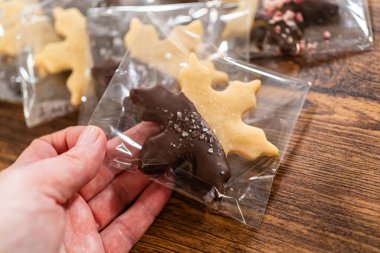 Dikkatlice paketlenmiş Noel kurabiyeleri, çikolataya batırılmış ve şeffaf selofan ambalajla sunulmuş, bayram hediyesi olarak mükemmel..