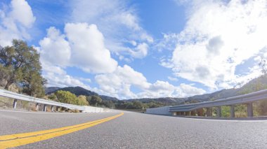 Araç, parlak güneşin altında Cuyama Otoyolu boyunca ilerliyor. Çevresindeki manzara, ışık saçan güneş ışığıyla aydınlanır ve araba seyahat ederken güzel ve davetkar bir sahne yaratır.