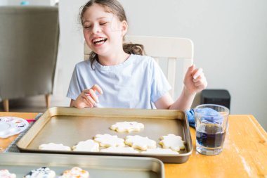 Küçük bir kızın özenle yazdığı iç açıcı bir sahne. Şekerli kurabiyelerin üzerine besin boyası sürmüş. Kurabiyeler güzel bir şekilde beyaz kraliyet kreması ile dolmuş..