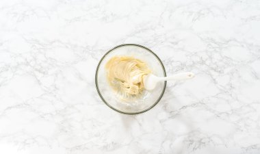 Düz yatıyordu. Mayasız tarçınlı çörekler için krem peynirli krema yapmak için karıştırma kabındaki malzemeleri karıştırıyorum..