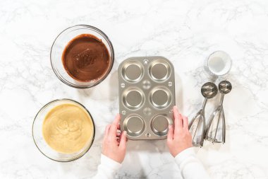 Düz yatıyordu. Cupcake folyoları titizlikle hem çikolata hem de vanilya hamuruyla dolduruluyor. Lezzetli çeşitlilikte doğum günü kekleri pişirmek için zemin hazırlıyorlar..