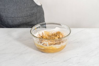 Islak ve kuru malzemelerle karıştırılmış cam bir kabın içinde çırpılmış beyaz çikolatalı makadamia fındığı..