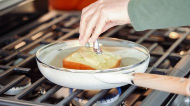 Modern beyaz bir mutfak, muz dilimleri ve brioche ekmek cızırtısı içinde gaz sobasının üzerinde, baştan çıkarıcı bir ızgara fıstık ezmeli muzlu sandviç için zemin hazırlıyor..