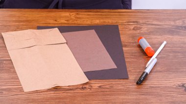 Adım adım. Öğretmen, kahverengi bir çantadan kağıt bir kukla yaparak, çalışma alanı olarak ahşap bir yüzey kullanarak çevrimiçi sınıfa rehberlik ediyor..