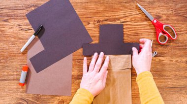 Adım adım. Düz yatıyordu. Öğretmen, kahverengi bir çantadan kağıt bir kukla yaparak, çalışma alanı olarak ahşap bir yüzey kullanarak çevrimiçi sınıfa rehberlik ediyor..