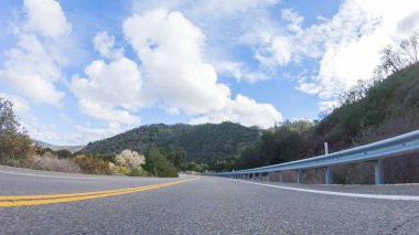 Araç, parlak güneşin altında Cuyama Otoyolu boyunca ilerliyor. Çevresindeki manzara, ışık saçan güneş ışığıyla aydınlanır ve araba seyahat ederken güzel ve davetkar bir sahne yaratır.