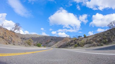 Araç, parlak güneşin altında Cuyama Otoyolu boyunca ilerliyor. Çevresindeki manzara, ışık saçan güneş ışığıyla aydınlanır ve araba seyahat ederken güzel ve davetkar bir sahne yaratır.