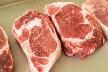 Modern beyaz bir mutfakta, baharatlı bir pirzola bifteği, güzel mermerleriyle övünerek, bir pişirme çarşafının üzerinde oturur. Açık hava gaz ızgarası için hazırlanıyor, mükemmel bir kavurucu söz veriyor.