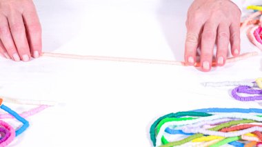 Eller birbirine zıt beyaz bir yüzeye karşı düzgün düzenlenmiş renkli, sarmalanmış kil boncuk iplikçiklerine dokunur..