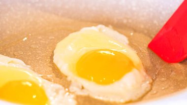 Canlı yumurta sarıları parlıyor, kırmızı spatula benekli tavada yumurta pişiriyor..
