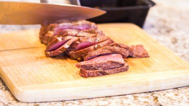 Eldivenli şef lezzetli pembe bifteği doğal bambu tahtasında, mutfak zemininde dilimliyor..