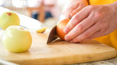 Modern bir mutfağın hoş geldin ortamında genç bir adam akşam yemeği hazırlama sürecine devam ediyor. Şu anda sarı soğanları halka şeklinde dilimleyip ızgara yapmaya hazırlanıyor.