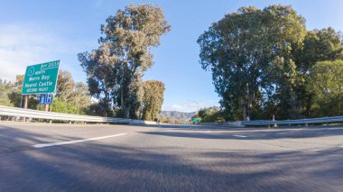 Kış günü San Luis Obispo, Kaliforniya yakınlarındaki ikonik 1. Otoyol boyunca bir araba gider. Çevresindeki manzara kahverengimsi ve bastırılmış, dalgalı tepeler ve kıyı şeritleriyle