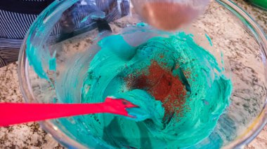 İyi ışıklandırılmış bir mutfakta, yeşil ve diğer renklerin çeşitli tonlarında tereyağlı krema çeşitleri büyüleyici kapkeklerin sanatsal dekorasyonu için titizlikle karıştırılıyor ve hazırlanıyor.