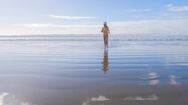 Küçük kız, soğuğa göğüs geriyor, kışın sahilde mayosuyla koşuyor..