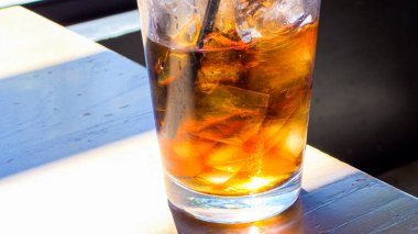 Yakından çekilen bir resimde buz ve gazoz dolu ferahlatıcı bir bardak bir restoran masasına yerleştirilir ve izleyicileri serin ve köpüklü bir içecek içmeye davet edilir..