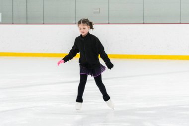 Artistik patinaj rutinini mükemmelleştiren genç bir kız kapalı bir buz pateni sahasında yarışma elbisesini giyerken.