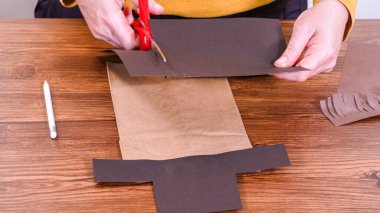 Adım adım. Öğretmen, kahverengi bir çantadan kağıt bir kukla yaparak, çalışma alanı olarak ahşap bir yüzey kullanarak çevrimiçi sınıfa rehberlik ediyor..