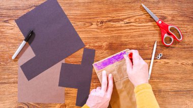 Adım adım. Düz yatıyordu. Öğretmen, kahverengi bir çantadan kağıt bir kukla yaparak, çalışma alanı olarak ahşap bir yüzey kullanarak çevrimiçi sınıfa rehberlik ediyor..