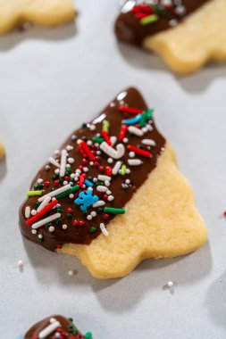 Çikolataya yarı batırılmış tereyağlı kurabiyeler, üzerine kırmızı, yeşil ve beyaz süslemeler serpiştirilmiş beyaz parşömen üzerine serpiştirilmiş..
