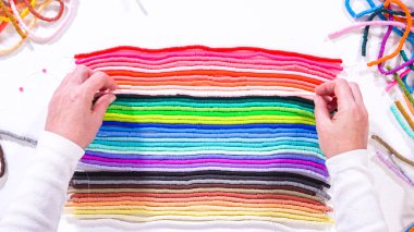 Düz yatıyordu. Eller birbirine zıt beyaz bir yüzeye karşı düzgün düzenlenmiş renkli, sarmalanmış kil boncuk iplikçiklerine dokunur..