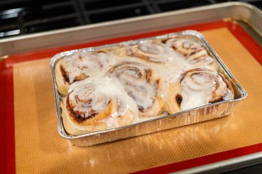 Fırından yeni çıkmış, tarçınlı çörek silikon bir hasırın üzerinde serinliyor, kremaları mutfak ışıklarının altında parlıyor..