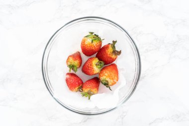 Parlak kırmızı çilekler, küf izleriyle karışmış, beyaz peçetedeki kağıt havluyla kaplı cam bir kasede dinleniyor, depolama tekniklerini gösteriyor..