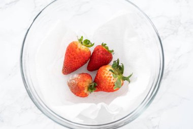 Parlak kırmızı çilekler, küf izleriyle karışmış, beyaz peçetedeki kağıt havluyla kaplı cam bir kasede dinleniyor, depolama tekniklerini gösteriyor..