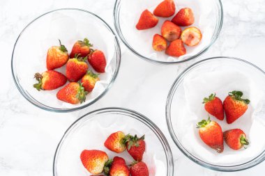 Parlak kırmızı çilekler, küf izleriyle karışmış, beyaz peçetedeki kağıt havluyla kaplı cam bir kasede dinleniyor, depolama tekniklerini gösteriyor..