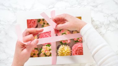 Düz yatıyordu. Bir kadının ellerinde, her biri canlı güller ve krema kaplamasından yapılmış lalelerle süslenmiş gurme keklerle dolu beyaz bir kağıt kutu nazikçe kapatılıyor..