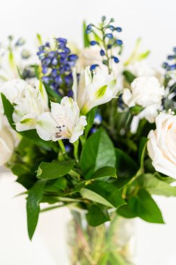 Taze beyaz güllerin ve çeşitli çiçeklerin bulunduğu büyüleyici bir buket, zarif bir vazoda düzenlenmiş, zamansız bir güzellik yayıyor..