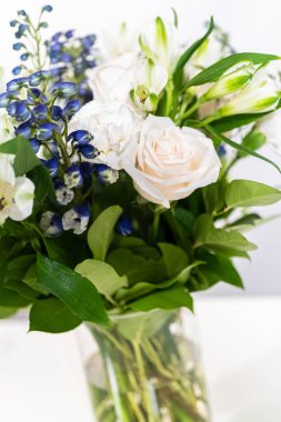 Taze beyaz güllerin ve çeşitli çiçeklerin bulunduğu büyüleyici bir buket, zarif bir vazoda düzenlenmiş, zamansız bir güzellik yayıyor..