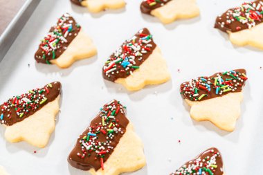 Çikolataya yarı batırılmış tereyağlı kurabiyeler, üzerine kırmızı, yeşil ve beyaz süslemeler serpiştirilmiş beyaz parşömen üzerine serpiştirilmiş..