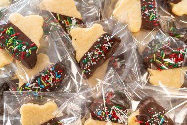 Dikkatlice paketlenmiş Noel kurabiyeleri, çikolataya batırılmış ve şeffaf selofan ambalajla sunulmuş, bayram hediyesi olarak mükemmel..