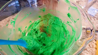 İyi ışıklandırılmış bir mutfakta, yeşil ve diğer renklerin çeşitli tonlarında tereyağlı krema çeşitleri büyüleyici kapkeklerin sanatsal dekorasyonu için titizlikle karıştırılıyor ve hazırlanıyor.