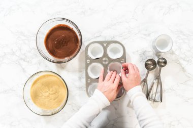 Düz yatıyordu. Cupcake folyoları titizlikle hem çikolata hem de vanilya hamuruyla dolduruluyor. Lezzetli çeşitlilikte doğum günü kekleri pişirmek için zemin hazırlıyorlar..
