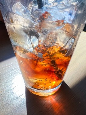 Yakından çekilen bir resimde buz ve gazoz dolu ferahlatıcı bir bardak bir restoran masasına yerleştirilir ve izleyicileri serin ve köpüklü bir içecek içmeye davet edilir..