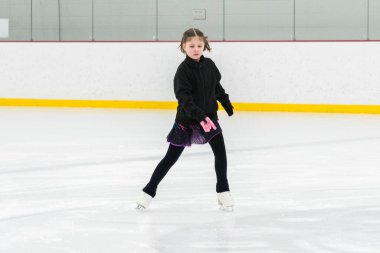 Artistik patinaj rutinini mükemmelleştiren genç bir kız kapalı bir buz pateni sahasında yarışma elbisesini giyerken.