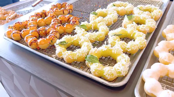 Metal tepsilerde çeşitli malzemelerle taze pişmiş mochi çörekleri eşsiz şekillerini ve şekerli kaplamalarını vurguluyor..