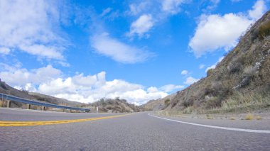 Araç, parlak güneşin altında Cuyama Otoyolu boyunca ilerliyor. Çevresindeki manzara, ışık saçan güneş ışığıyla aydınlanır ve araba seyahat ederken güzel ve davetkar bir sahne yaratır.