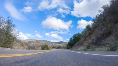 Araç, parlak güneşin altında Cuyama Otoyolu boyunca ilerliyor. Çevresindeki manzara, ışık saçan güneş ışığıyla aydınlanır ve araba seyahat ederken güzel ve davetkar bir sahne yaratır.