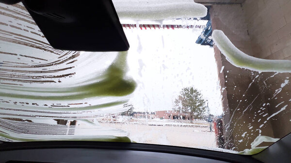 Soapy windshield view from inside a car during an automatic wash cycle, with the foam obscuring the outside.