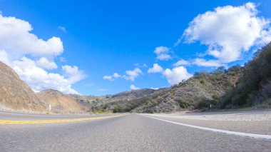 Araç, parlak güneşin altında Cuyama Otoyolu boyunca ilerliyor. Çevresindeki manzara, ışık saçan güneş ışığıyla aydınlanır ve araba seyahat ederken güzel ve davetkar bir sahne yaratır.