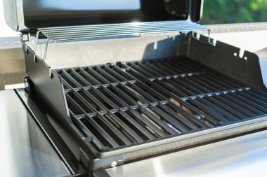 Yakından bakıldığında, banliyödeki bir evin balkonunda ilk açık hava yemek pişirme macerasını bekleyen iki ocaklı ızgaranın bozulmamış ızgarasını gösteriyor..