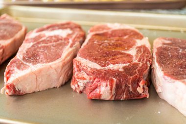 Modern beyaz bir mutfakta, baharatlı bir pirzola bifteği, güzel mermerleriyle övünerek, bir pişirme çarşafının üzerinde oturur. Açık hava gaz ızgarası için hazırlanıyor, mükemmel bir kavurucu söz veriyor.