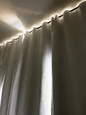 Sıcak güneş ışığı, yoğun karartma perdelerinin kenarlarından süzülerek dinlenme odasının sessiz boşluğunda huzur dolu bir parıltı sunar..