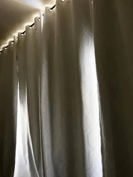 Warm sunlight filters through the edges of heavy blackout curtains, offering a tranquil glow in the quiet space of a restful room.