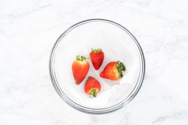 Parlak kırmızı çilekler, küf izleriyle karışmış, beyaz peçetedeki kağıt havluyla kaplı cam bir kasede dinleniyor, depolama tekniklerini gösteriyor..